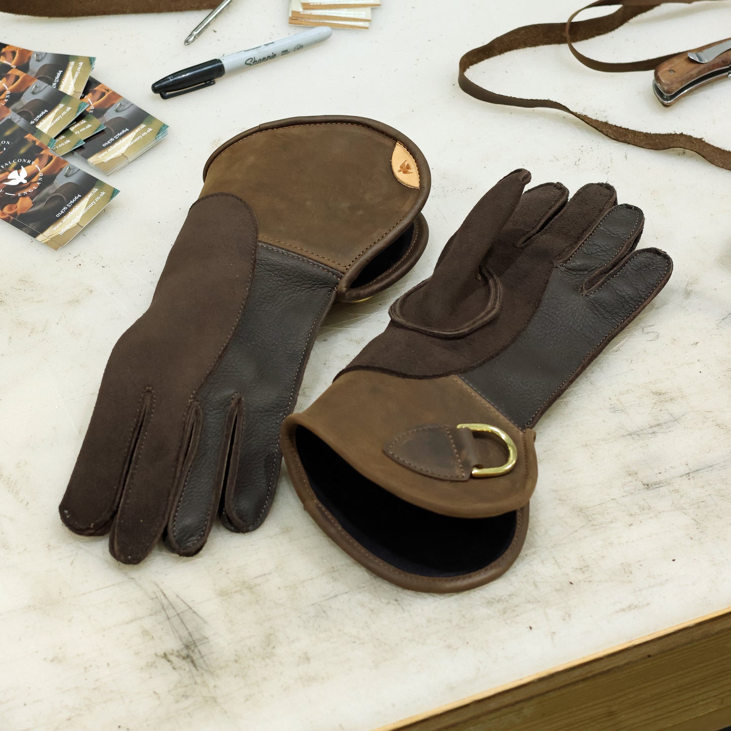 Brown double thickness deerskin falconry gloves showing the palm and back on a workshop bench