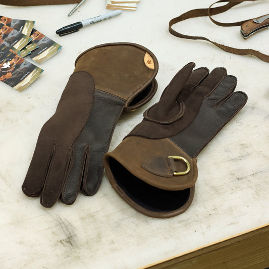 Brown double thickness deerskin falconry gloves showing the palm and back on a workshop bench