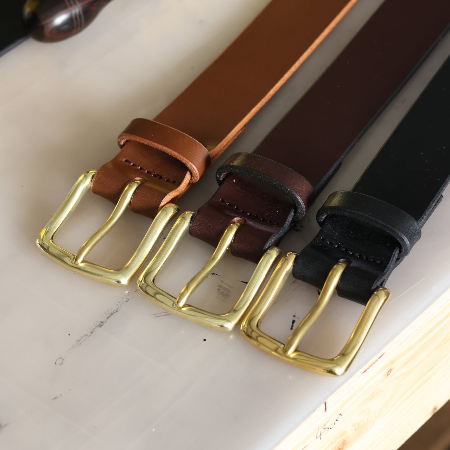 Three leather belts with brass buckles on a work bench