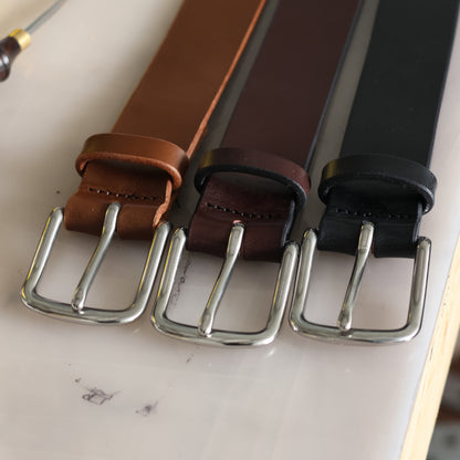 Three belts with different colors and stainless steel buckles on a light surface.