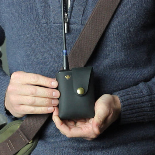 Person holding a black leather pouch with a brown strap against a blurred background